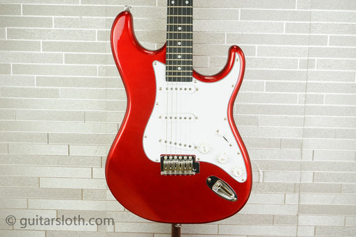 Red electric guitar on a stand against a light gray tiled wall